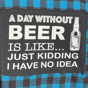 May include: A black patch with white text that reads "A day without beer is like... Just kidding I have no idea." A cartoon image of a bottle of beer is to the right of the text.