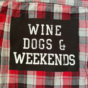 May include: Red and black plaid flannel shirt with a black patch that says "Wine Dogs & Weekends" in white lettering.