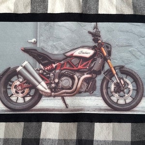 May include: A black and red motorcycle with the word "Indian" on the gas tank. The motorcycle is parked in front of a gray wall with a door.