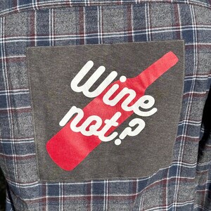 May include: A gray and red plaid flannel shirt with a patch on the back that says "Wine not?" in white text with a red wine bottle graphic.