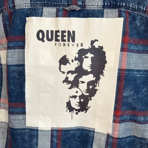 May include: A blue and red plaid flannel shirt with a white patch featuring a black silhouette of the band Queen and the text "QUEEN FOREVER".