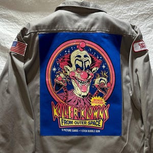 May include: A gray work shirt with a blue patch featuring a cartoon of a scary clown with red hair and a pink collar. The patch says "Killer Klowns from Outer Space" and "9 Picture Cards + 1 Stick Bubble Gum". There is a small red sticker that says "Bonus Sticker!" on the patch. There is a small American flag patch on the left sleeve and a small red and white patch that says "Safe First" on the right sleeve.