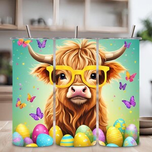 Puede incluir: Tres vasos de acero inoxidable con un diseño de una vaca de las Highlands con gafas de sol amarillas y rodeada de huevos de Pascua coloridos y mariposas sobre un fondo turquesa.
