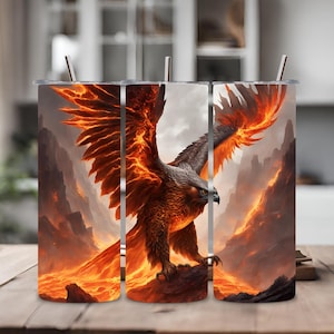 Puede incluir: Un vaso de acero inoxidable con un diseño de un fénix llameante con llamas naranjas y amarillas. El fénix está posado en un acantilado rocoso con un fondo de paisaje llameante.