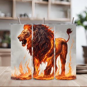 Puede incluir: Tres vasos de acero inoxidable con un diseño de un león de pie en llamas. El león es naranja y marrón con una melena espesa de fuego.