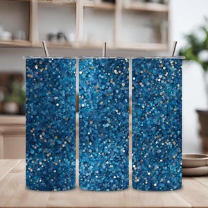 Puede incluir: Tres vasos de acero inoxidable con patrones de purpurina azul. Los vasos están alineados en una fila sobre una superficie de madera.