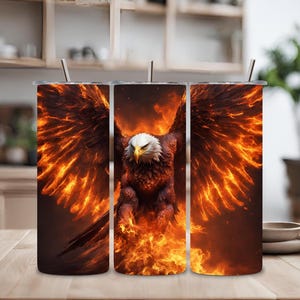 Puede incluir: Tres vasos de acero inoxidable con un diseño de un águila con las alas extendidas, volando a través de las llamas. El águila es marrón y blanca, y las llamas son naranja y amarillas.