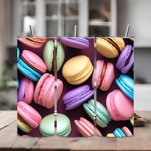 Puede incluir: Cuatro vasos de acero inoxidable con un patrón de macarons coloridos. Los vasos tienen un fondo morado y presentan macarons de varios colores, incluyendo rosa, azul, amarillo y verde.