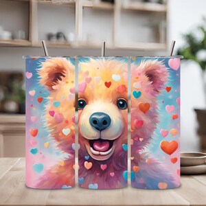 Puede incluir: Tres vasos de acero inoxidable con un diseño rosa, azul y blanco que presenta un oso de dibujos animados con corazones. El oso sonríe y tiene ojos azules.