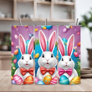 Puede incluir: Tres vasos de acero inoxidable con fondo morado, azul y rosa con un conejo blanco con pajarita y huevos de Pascua.