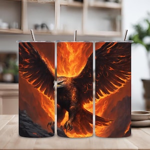 Puede incluir: Tres vasos de acero inoxidable con un diseño de un fénix que surge de las llamas. El fénix se representa con las alas extendidas, y las llamas son de un naranja y amarillo vibrantes.