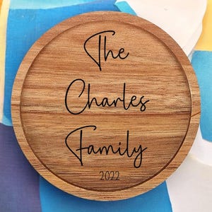May include: A round wooden coaster with the text "The Charles Family 2022" engraved in black.