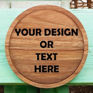 May include: A round wooden sign with the text "YOUR DESIGN OR TEXT HERE" in black lettering.