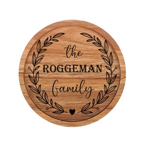 May include: A round wooden sign with a wreath of leaves and the text "The Roggeman Family" in black lettering.