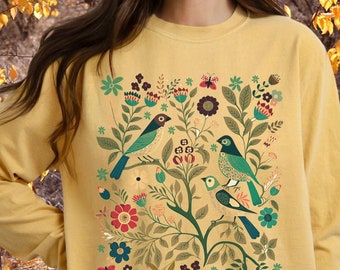 May include: A mustard yellow sweatshirt with a floral design featuring birds and leaves. The design is in shades of green, blue, red, and brown.
