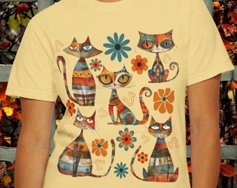 May include: A yellow t-shirt with a colorful print of cats and flowers. The cats are stylized and have different patterns and colors. The flowers are also colorful and have a variety of shapes.