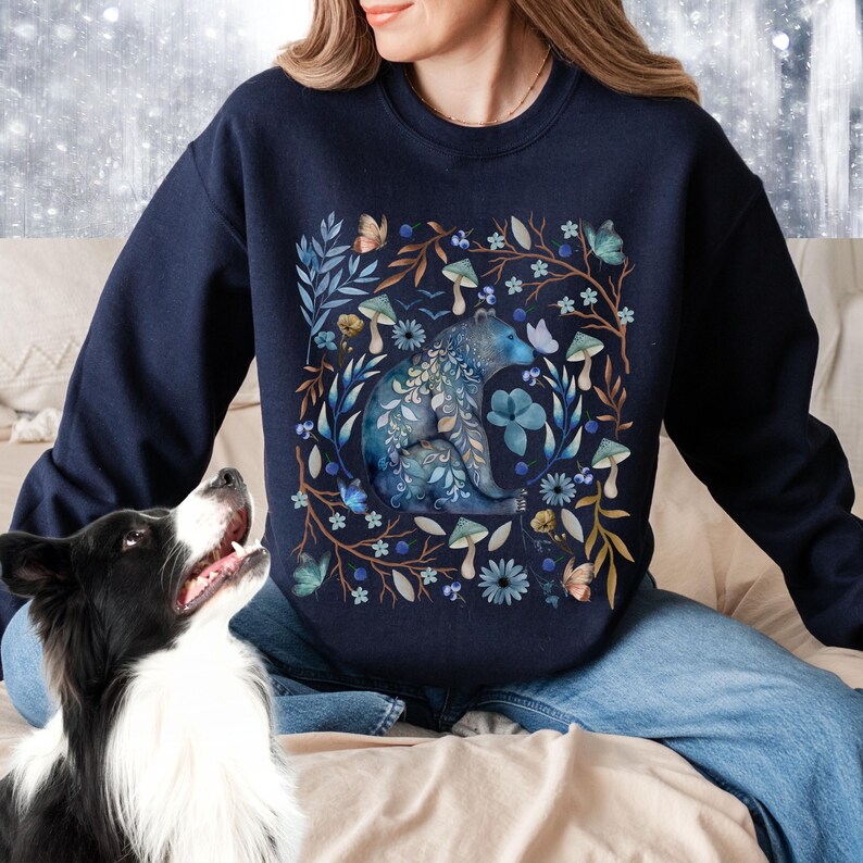 May include: A navy blue sweatshirt with a watercolor design of a bear surrounded by flowers, mushrooms, and butterflies.