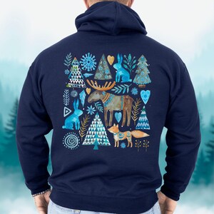 May include: Navy blue hoodie featuring a watercolor design of woodland creatures and trees. The design includes a moose, fox, rabbits, and stylized trees in shades of blue, gold, and brown. The hoodie has a drawstring hood and a kangaroo pocket.