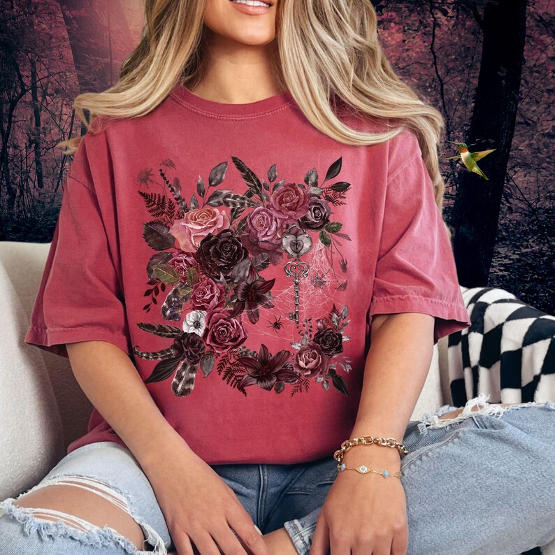 May include: A red oversized t-shirt with a floral design featuring dark red, pink, and white roses, leaves, and feathers. A key and spiderweb are also included in the design.