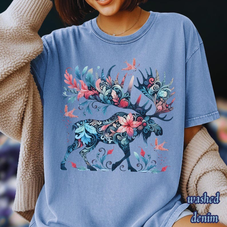 May include: A light blue t-shirt with a floral moose graphic. The moose is decorated with pink, blue, and teal flowers and leaves. The shirt has the words "washed denim" printed on the bottom right.