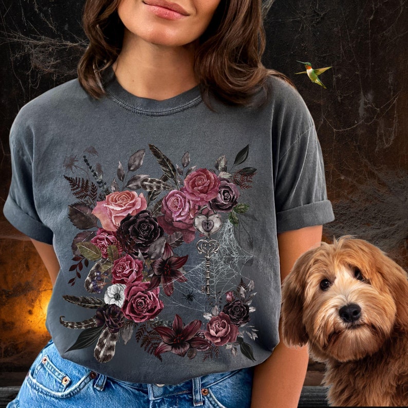 May include: A dark gray t-shirt with a floral design featuring dark red, pink, and purple roses, leaves, and feathers. A key and spiderwebs are also included in the design.