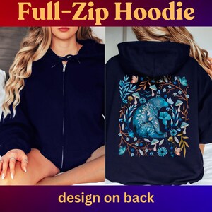 May include: Navy blue full-zip hoodie. The front features a full zipper closure. The back of the hoodie has a design with a blue bear surrounded by blue flowers, mushrooms, and butterflies. The text "Full-Zip Hoodie" and "design on back" are displayed.