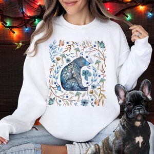 May include: White sweatshirt with a blue bear surrounded by watercolor flowers, leaves, and butterflies.