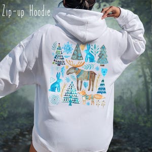 May include: White zip-up hoodie with a colorful winter-themed design on the back. The design features blue rabbits, trees, snowflakes, a moose, and a fox. The text "Zip-up Hoodie" is at the top left.