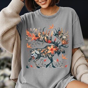 May include: Gray t-shirt featuring a detailed moose design with floral and leaf patterns in orange, white, and blue. The moose has large antlers and is surrounded by stylized birds and foliage.