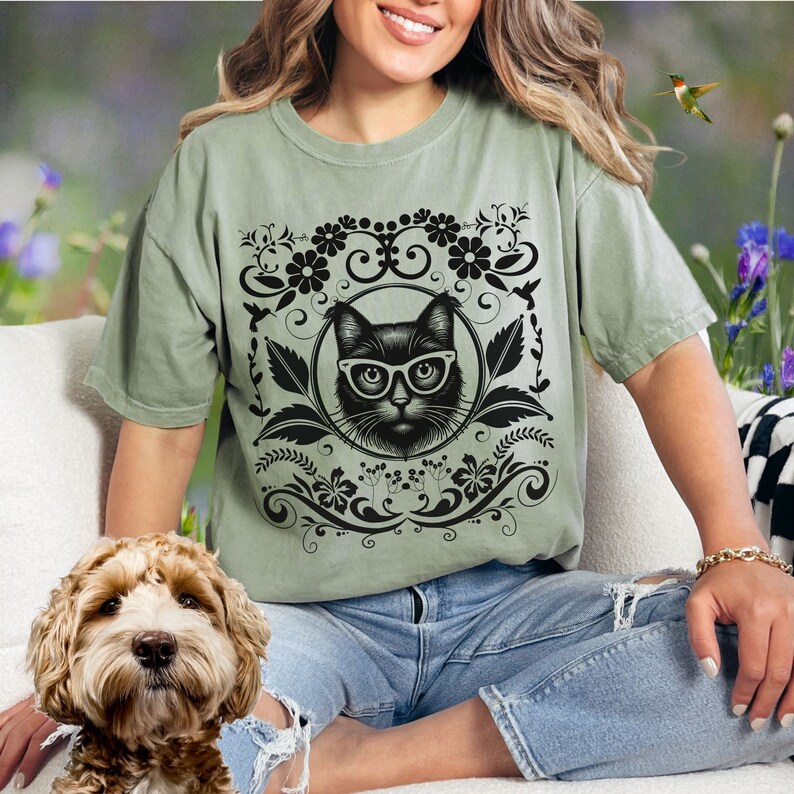 May include: A green t-shirt with a black cat wearing glasses in a floral design.