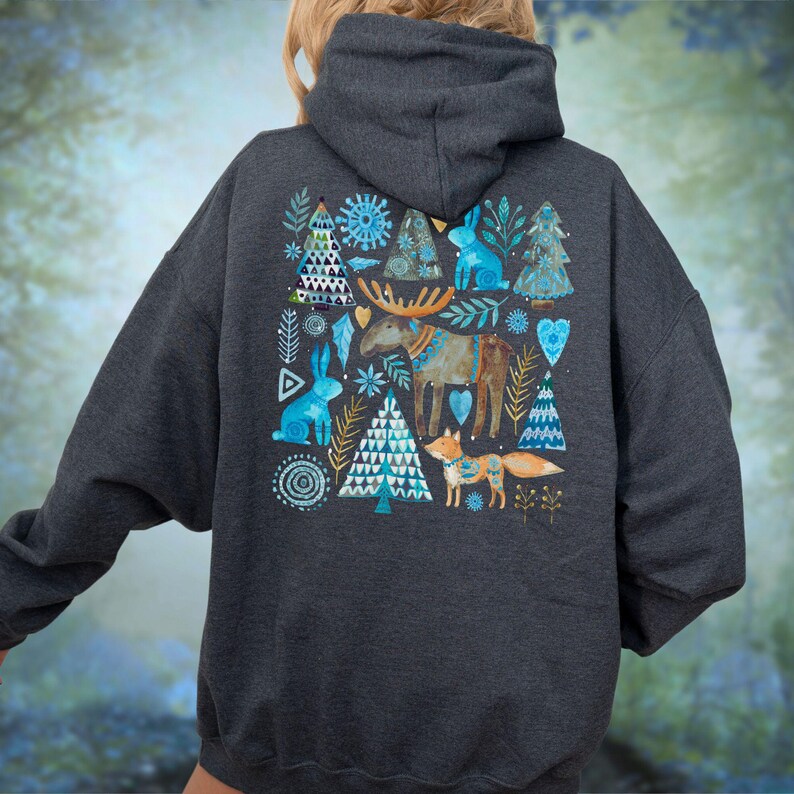 May include: Dark gray hoodie featuring a whimsical winter design on the back. The design includes blue rabbits, trees, a moose, and a fox. The artwork has a watercolor style with blue, white, and brown accents. The hoodie has a hood and long sleeves.