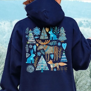 May include: Navy blue hooded sweatshirt featuring a winter-themed design on the back. The design includes a moose, fox, rabbits, and Christmas trees in shades of blue, brown, and gold. The sweatshirt has a drawstring hood and long sleeves.