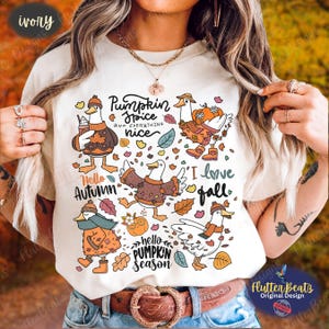 May include: An ivory t-shirt featuring a graphic print of five white ducks wearing autumn clothing like sweaters, scarves, and hats. The design includes pumpkins, falling leaves, and the text Pumpkin Spice and everything nice, Hello Autumn, I love fall, and hello PUMPKIN SEASON.
