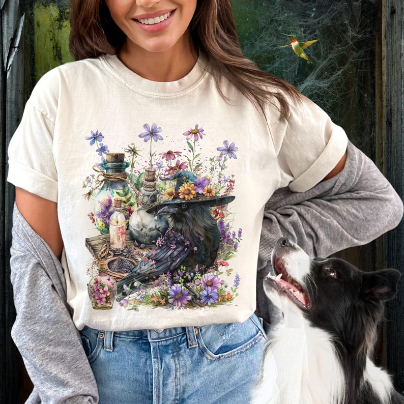 May include: A white t-shirt with a graphic print of a raven wearing a witch's hat surrounded by flowers and potion bottles.