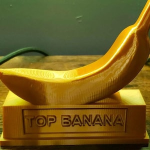 May include: A gold-colored banana-shaped trophy with the words "TOP BANANA" engraved on the base.