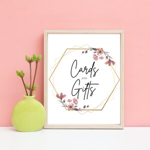 Puede incluir: Un cartel blanco con un marco geométrico dorado y detalles florales rosas. El cartel dice "Tarjetas y Regalos".