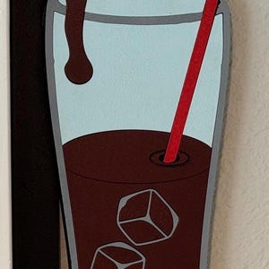 May include: A glass of iced coffee with a red straw and ice cubes. The coffee is pouring from a bottle cap.