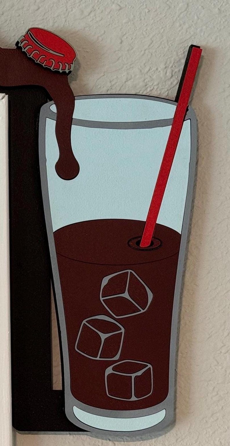 May include: A glass of iced coffee with a red straw and ice cubes. The coffee is pouring from a bottle cap.