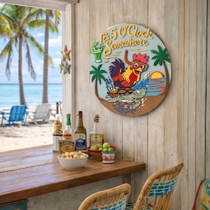 May include: A round wooden sign with the text "It's 5 O'Clock Somewhere" features a cartoon rooster wearing goggles riding a sea turtle. The sign is mounted on a white wooden wall, with a beach scene visible through a window.