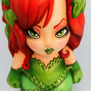 May include: A hand-painted ceramic figurine of Poison Ivy, a DC Comics supervillain. She has red hair, green leaves in her hair, and is wearing a green dress with a leafy design.