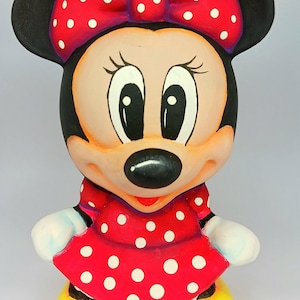 以下が含まれることがあります： 白い水玉模様の赤いドレスと白い水玉模様の赤いリボンをつけた、漫画のネズミのセラミック製フィギュア。ネズミは黒い耳、黒い鼻、大きな黒い目を持っている。