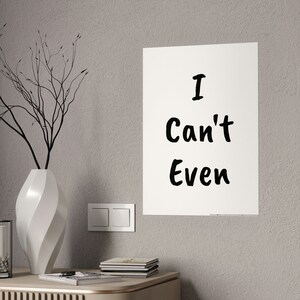 Peut inclure: Une affiche blanche avec du texte noir qui dit "I Can't Even". L'affiche est accrochée à un mur gris clair. Il y a un vase blanc avec une branche de brindilles dedans sur une table devant l'affiche.