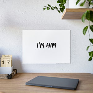 Peut inclure: Une affiche blanche avec du texte noir qui dit "I'M HIM" accrochée à un mur blanc.