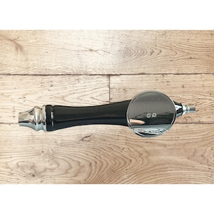 May include: A black and chrome beer tap handle with a circular chrome top. The handle has a sleek, modern design, with a polished chrome finish on the spout and accents. The tap handle is designed for dispensing beer.