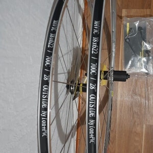 May include: Two silver bicycle wheels with black rims and white lettering. The lettering on the rims reads "MAVIC 18x622 / 700C / 28" OUTSIDE Nylon+PVC".