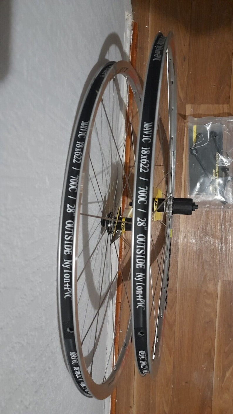 May include: Two silver bicycle wheels with black rims and white lettering. The lettering on the rims reads "MAVIC 18x622 / 700C / 28" OUTSIDE Nylon+PVC".