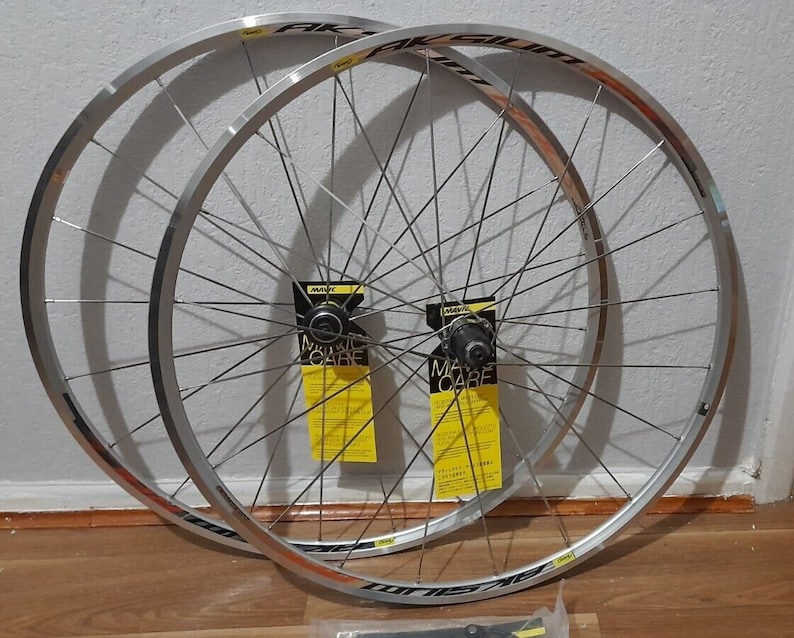May include: A pair of silver bicycle wheels with black spokes and black rim tape. The wheels are labelled "Aksium" and have yellow stickers with the text "Mavic Care".