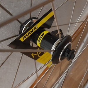 May include: Close-up of a silver bicycle wheel hub with a black Mavic label. The hub is surrounded by silver spokes.
