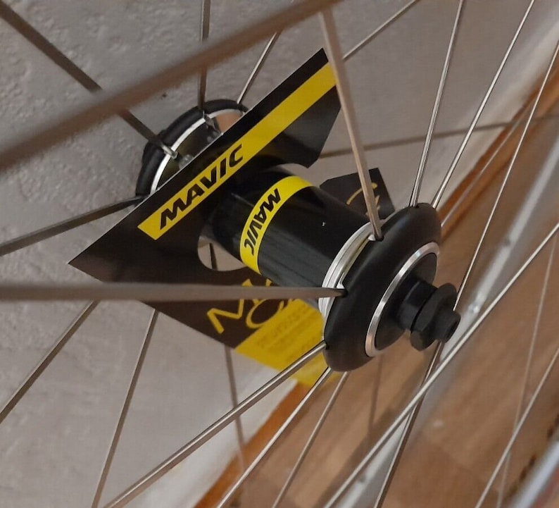 May include: Close-up of a silver bicycle wheel hub with a black Mavic label. The hub is surrounded by silver spokes.