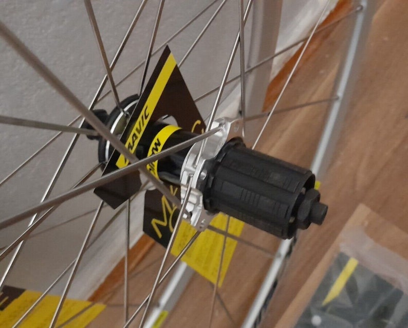 May include: Close-up of a silver bicycle wheel with black spokes and a black hub. The hub has a black Mavic logo on it.